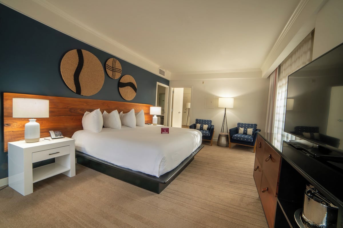 A hotel room with a large bed, bedside tables, a TV, and a seating area with chairs.