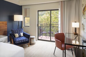 A hotel room with a blue armchair, a red chair, a glass table, and a balcony with chairs. - Amara Resort and Spa (Sedona)