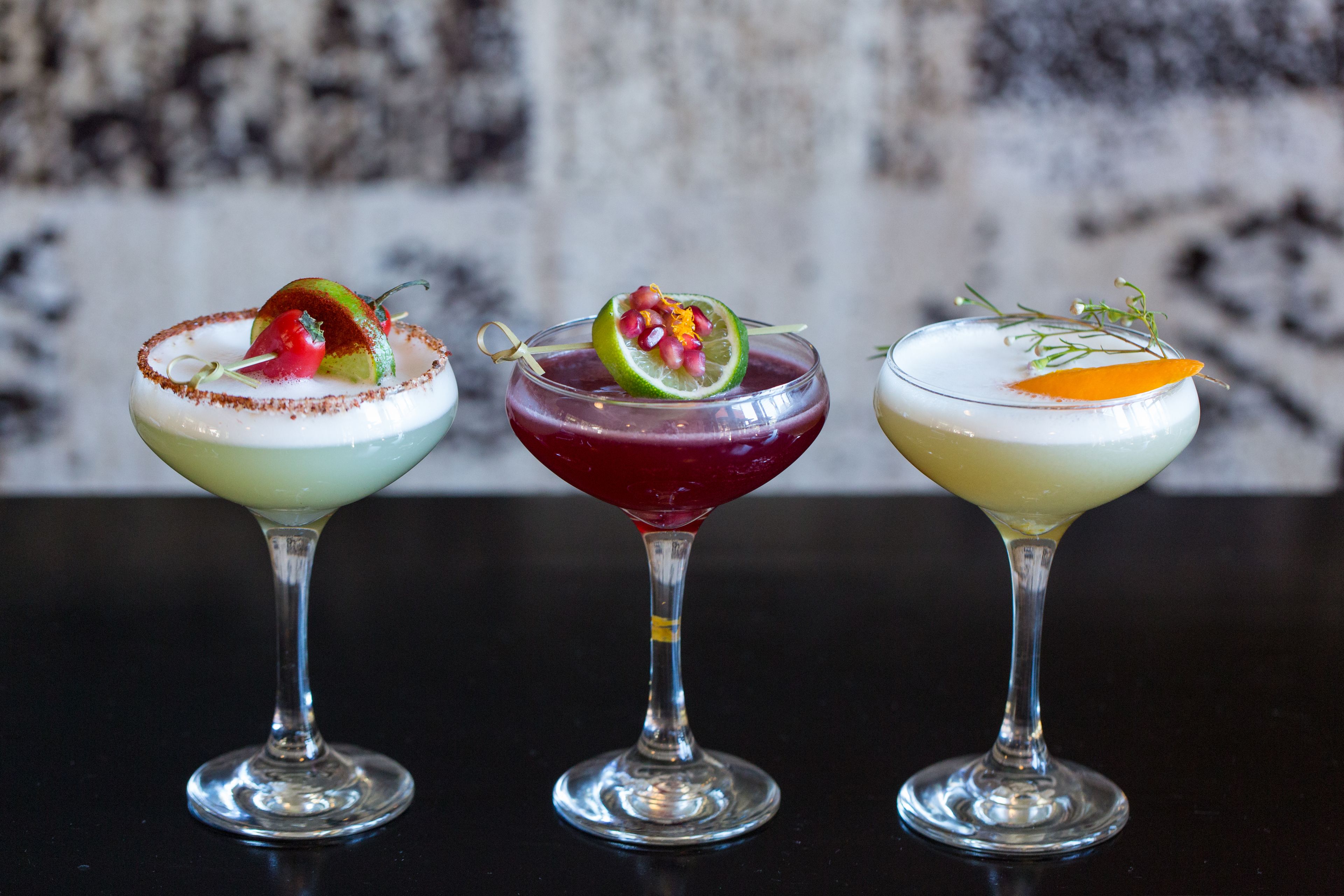 Trois cocktails, chacun agrémenté d’une garniture, sont présentés sur une surface sombre.
