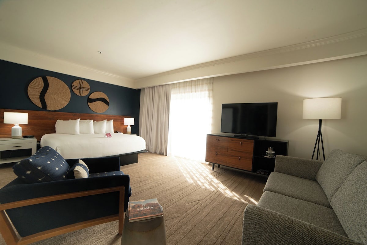 A hotel room with a bed, a TV, a desk, a chair, and a lamp.