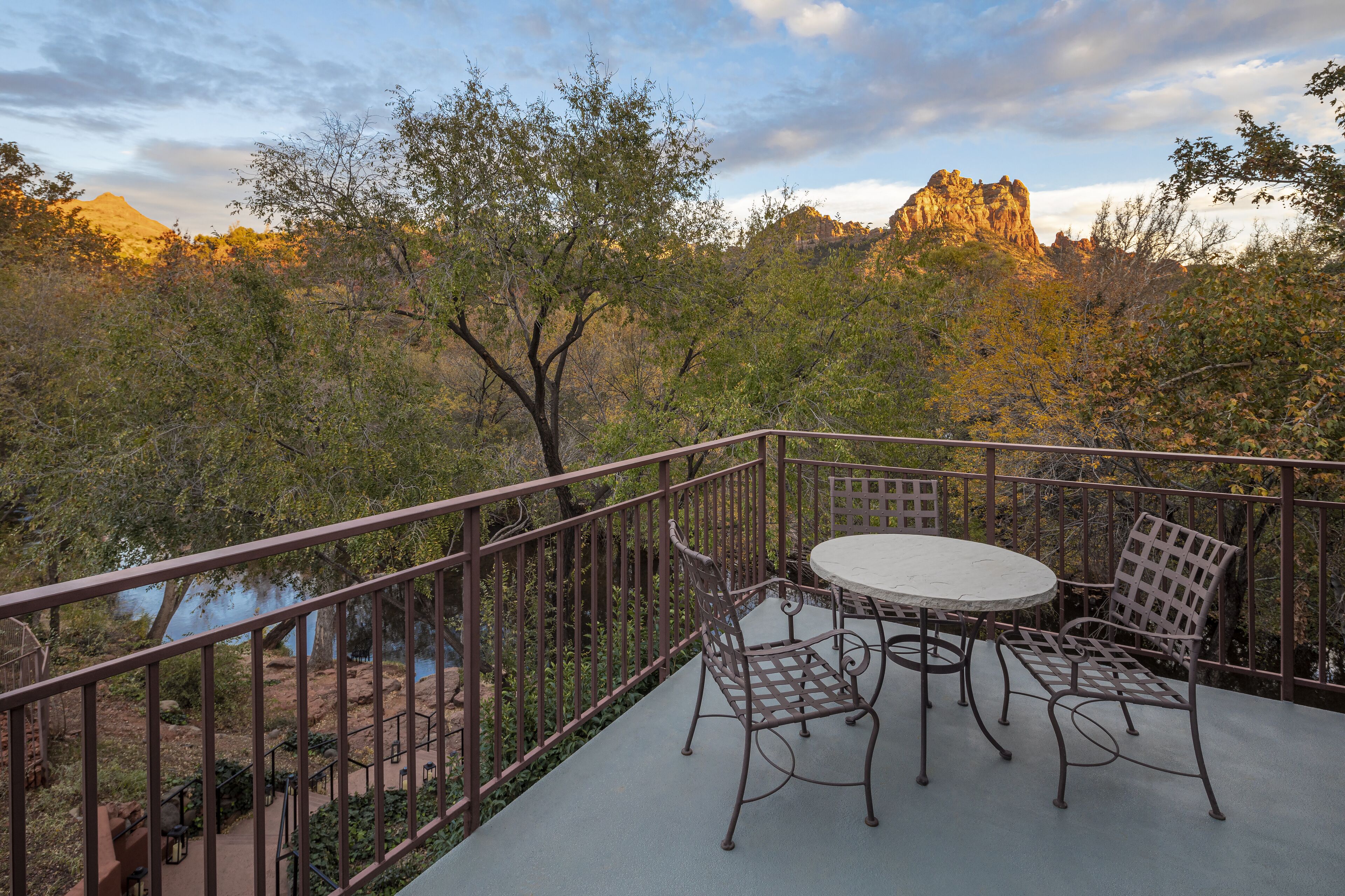 A balcony with a table and chairs, overlooking a natural landscape with trees and a mountain.