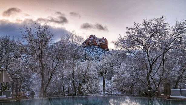 A serene winter scene with a clear pool reflecting trees and a distant mountain. - Amara Resort and Spa (Sedona)