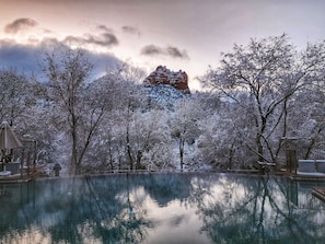 Escena invernal tranquila con una piscina cristalina que refleja árboles y una montaña distante.
