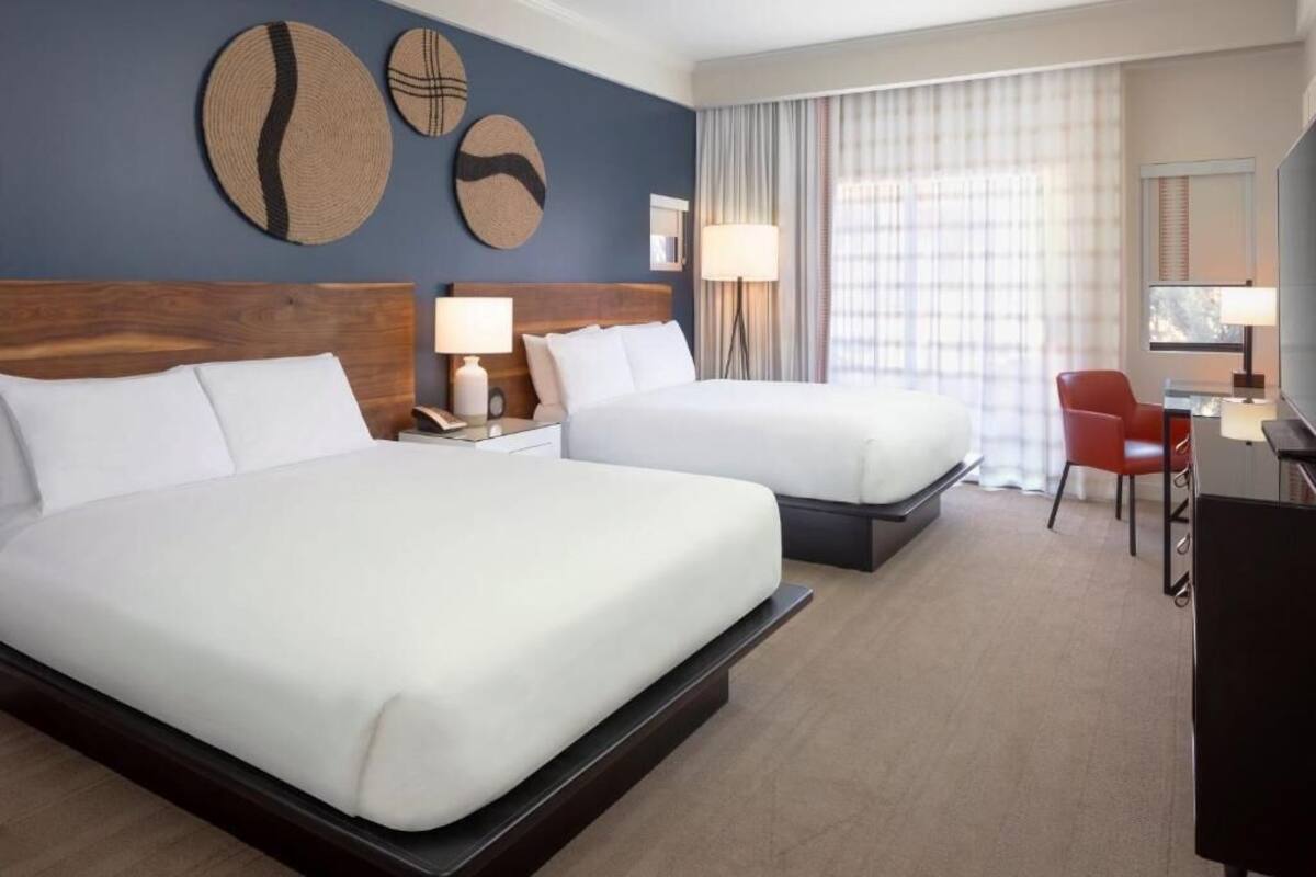 A hotel room with two beds, a desk, a chair, and a TV.