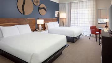 A hotel room with two beds, a desk, a chair, and a TV.