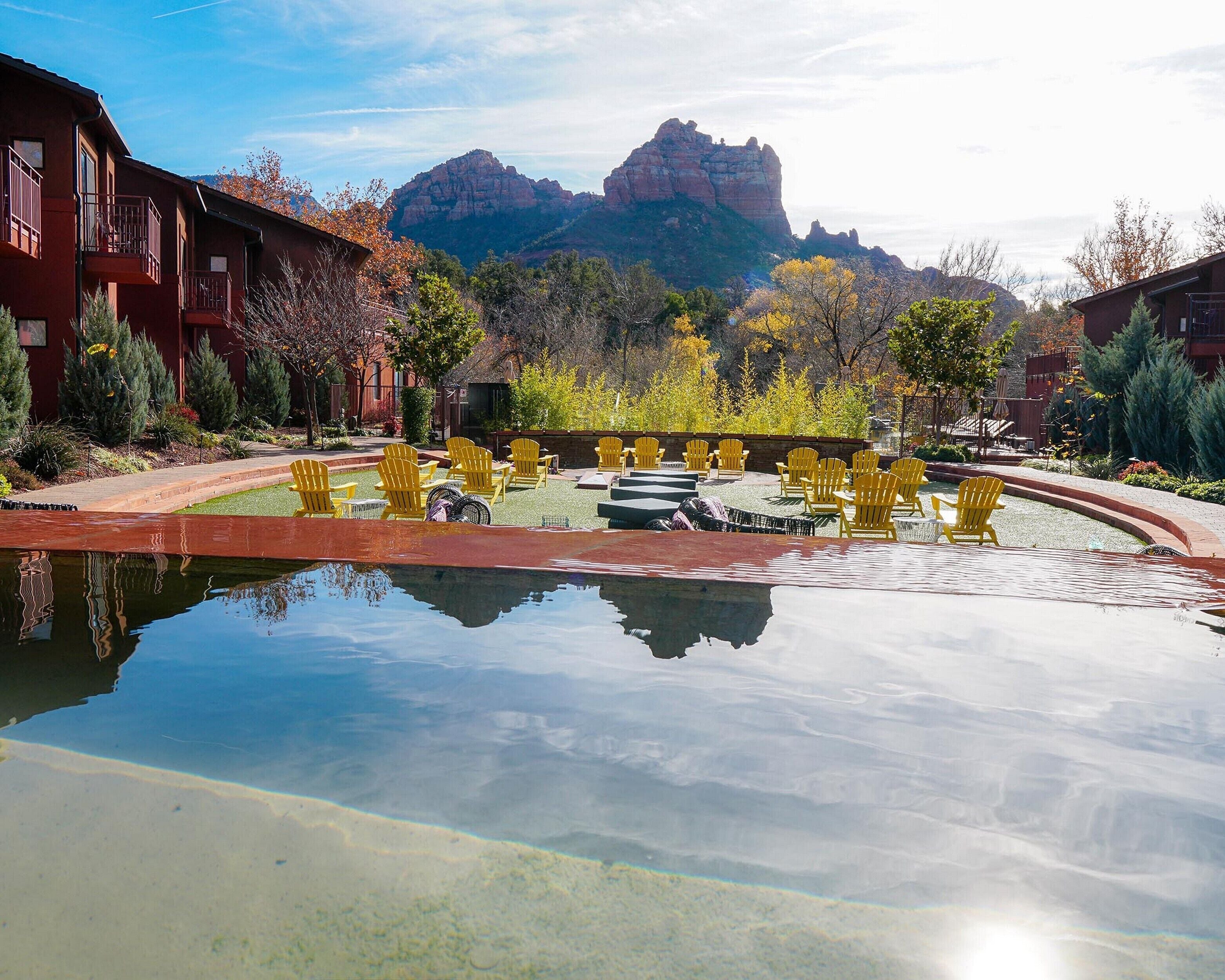 A pool with yellow chairs, a red building, and mountains in the background.