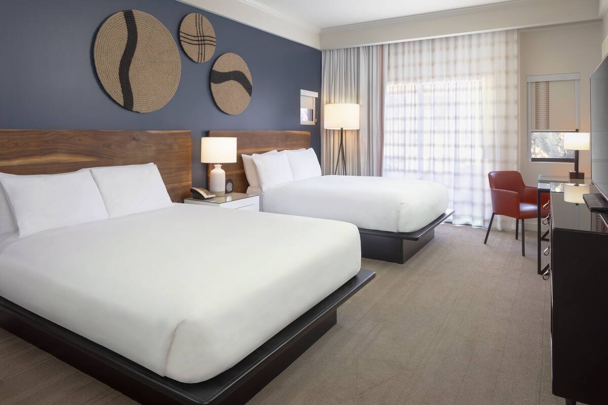 A hotel room with two beds, a desk, a chair, and a TV.