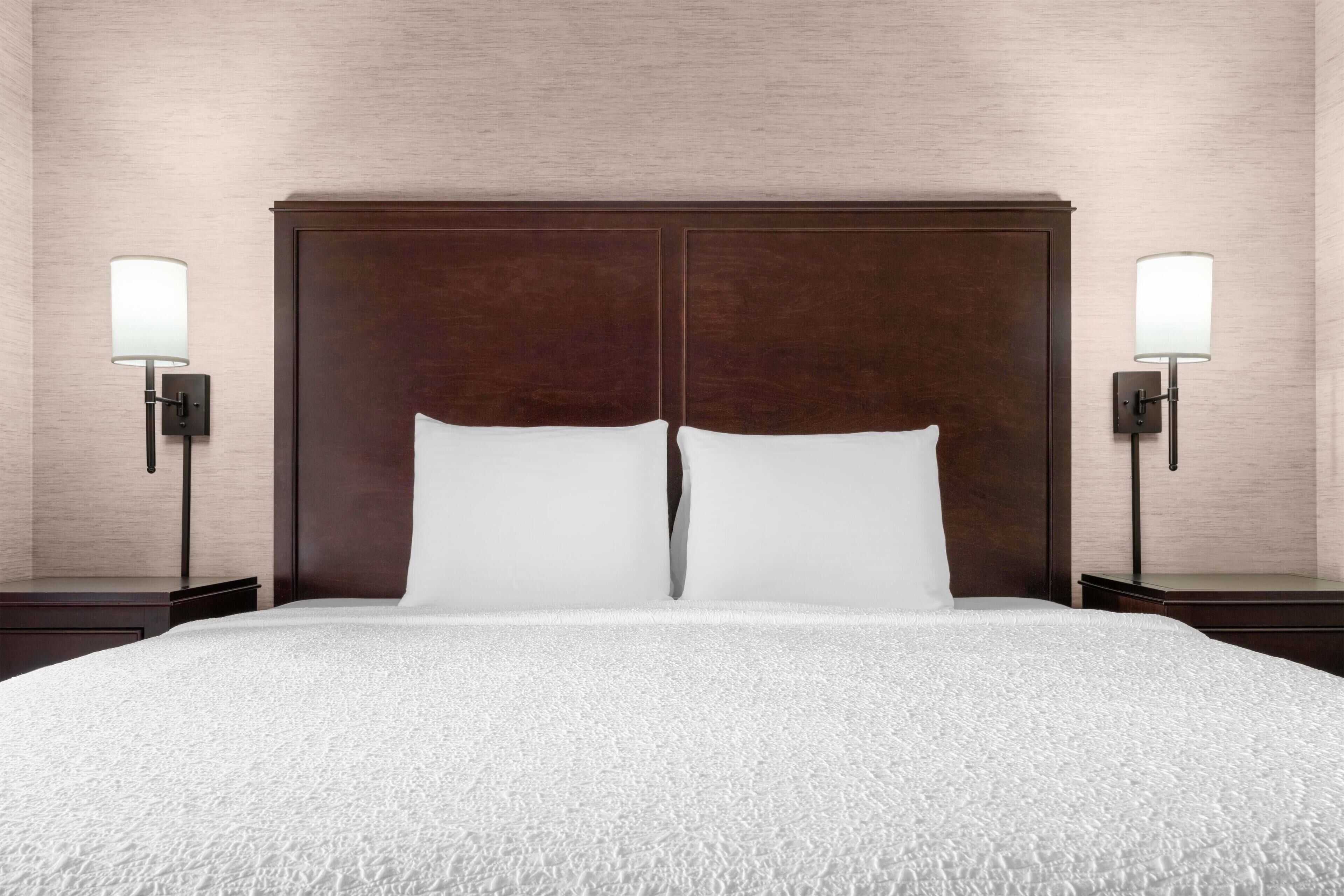 A hotel room with a large bed, two bedside lamps, and a wooden headboard.