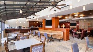 Un restaurant spacieux avec de hauts plafonds, des poutres apparentes et différents types de sièges, notamment des banquettes et des tables.