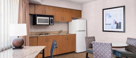 A compact hotel room with a kitchenette, a dining area with a table and chairs, and a framed picture on the wall.