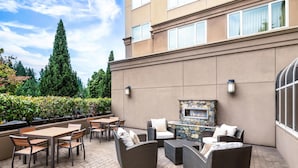 Une terrasse extérieure aménagée avec des meubles en osier, une cheminée en pierre et une vue sur la façade du bâtiment.