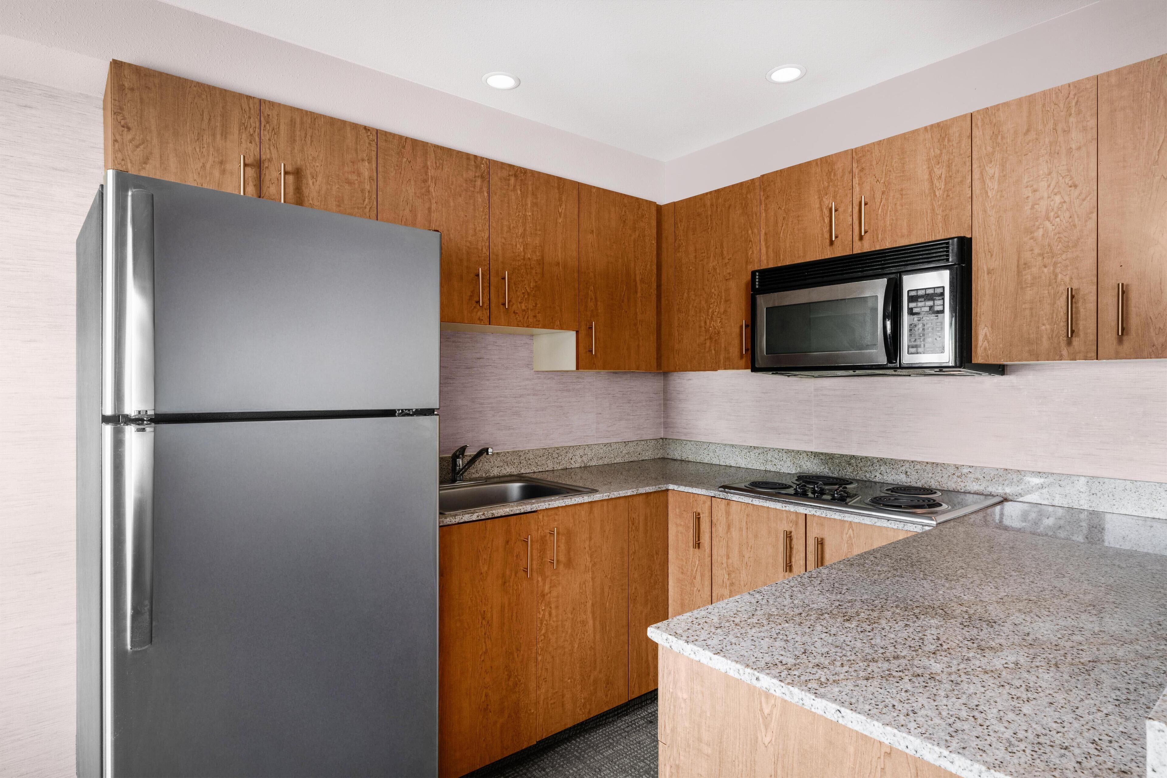 Una cocina con gabinetes de madera, electrodomésticos de acero inoxidable, encimeras de granito y un microondas integrado.
