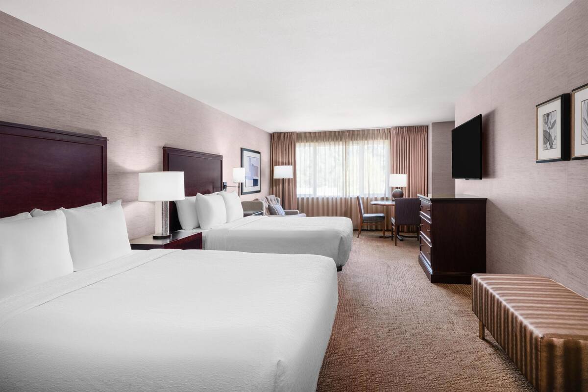 A hotel room with two beds, a desk, a chair, a television, and a window with curtains.