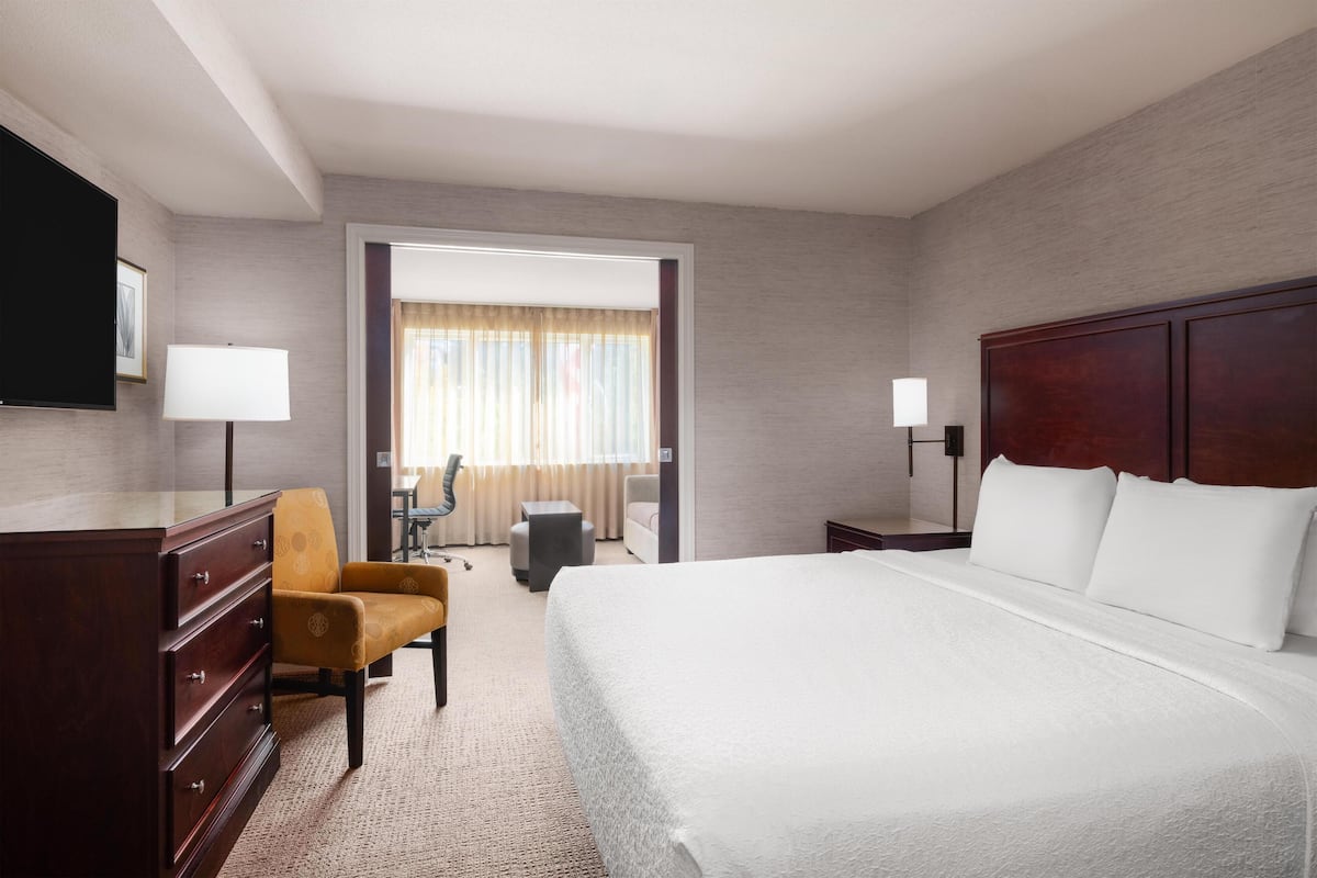 A hotel room with a large bed, a wooden dresser, a desk, a chair, and a television.