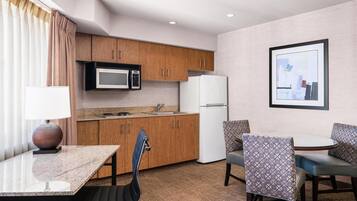 A compact hotel room with a kitchenette, a dining area with a table and chairs, and a single bed.