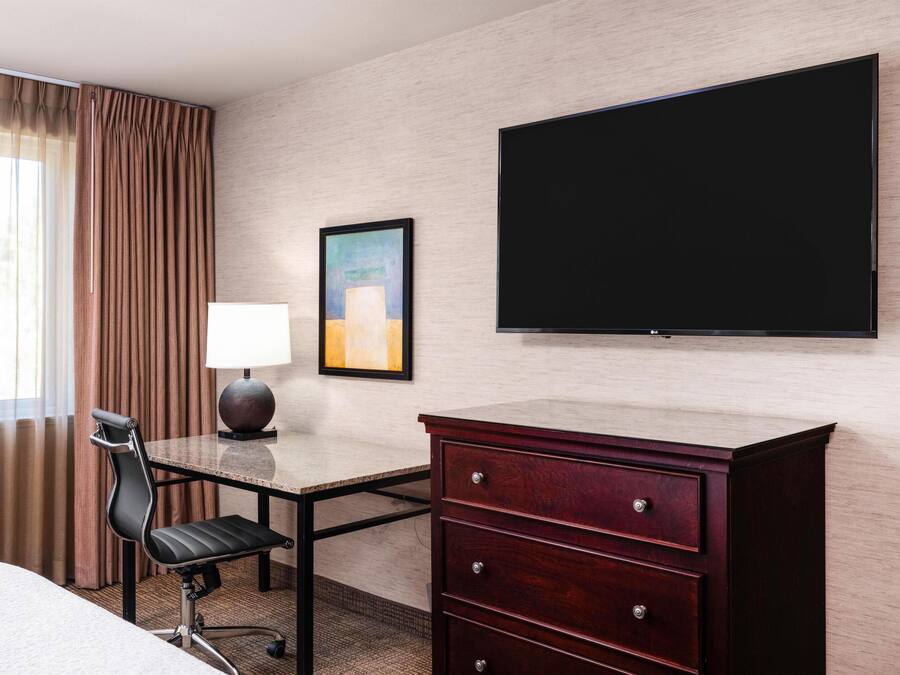 A hotel room with a desk, chair, and a flat-screen TV mounted on the wall.