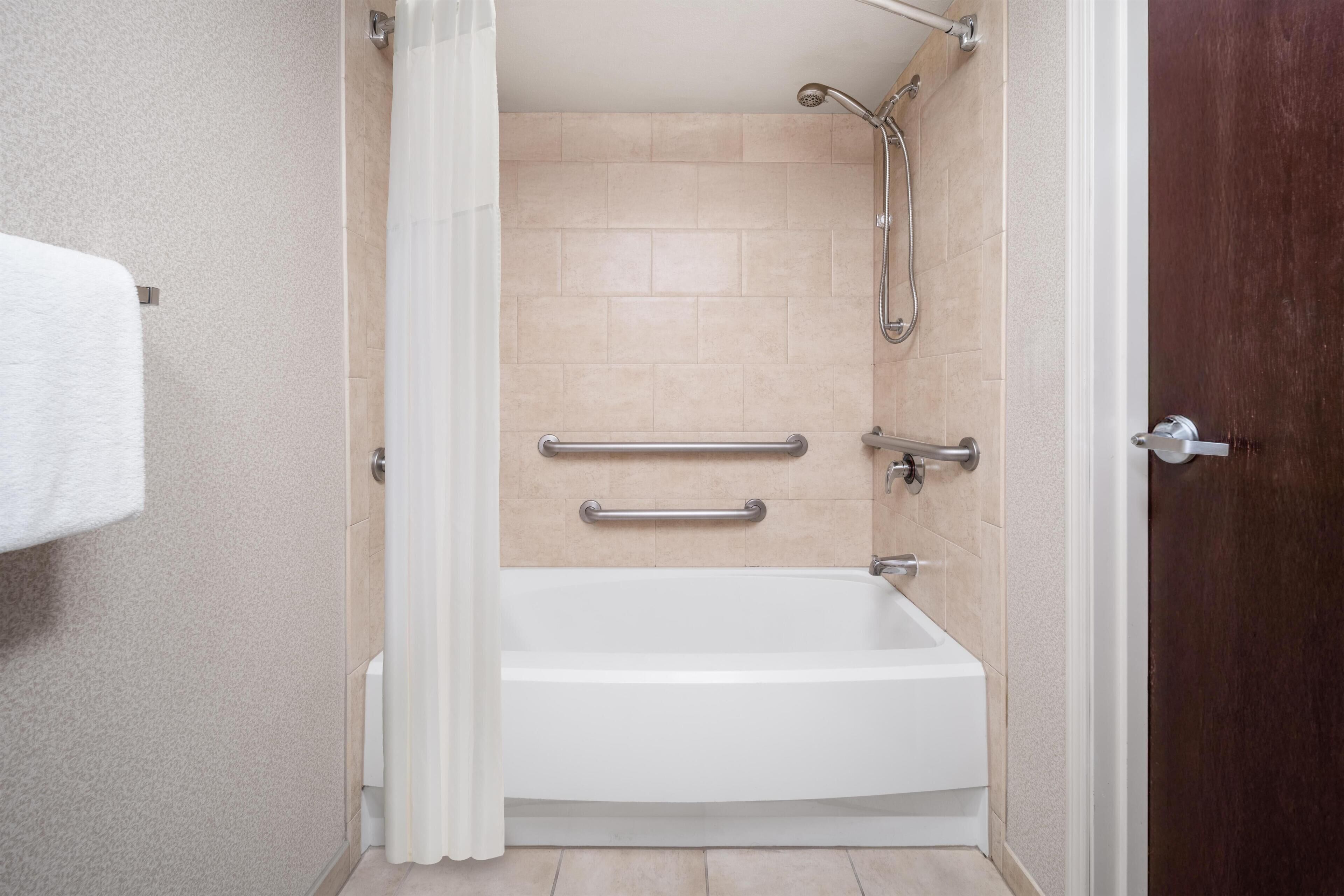 A bathroom with a white bathtub, beige tiles, a showerhead, and a door.