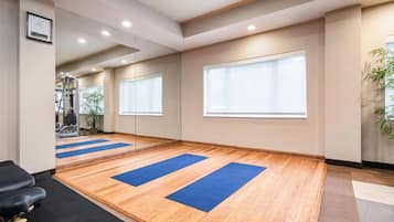Een ruime kamer met houten vloeren, grote ramen en yogamatten.