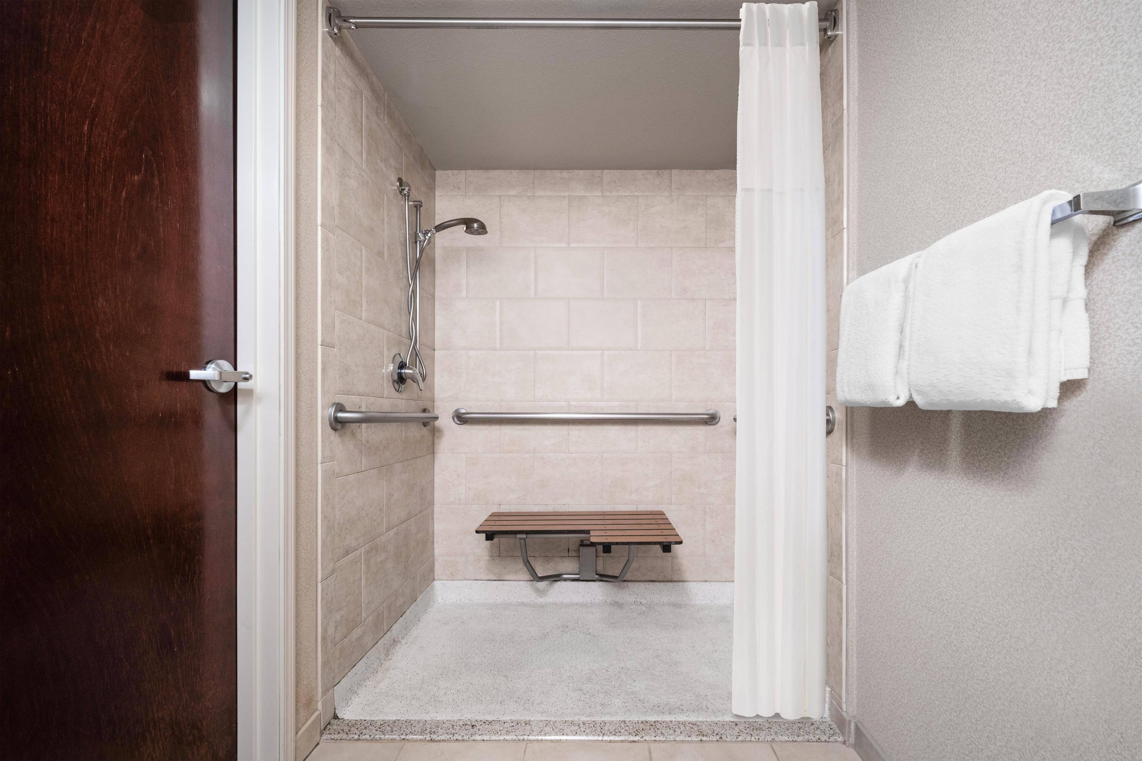 A shower stall with a bench, grab bars, and a towel rack.