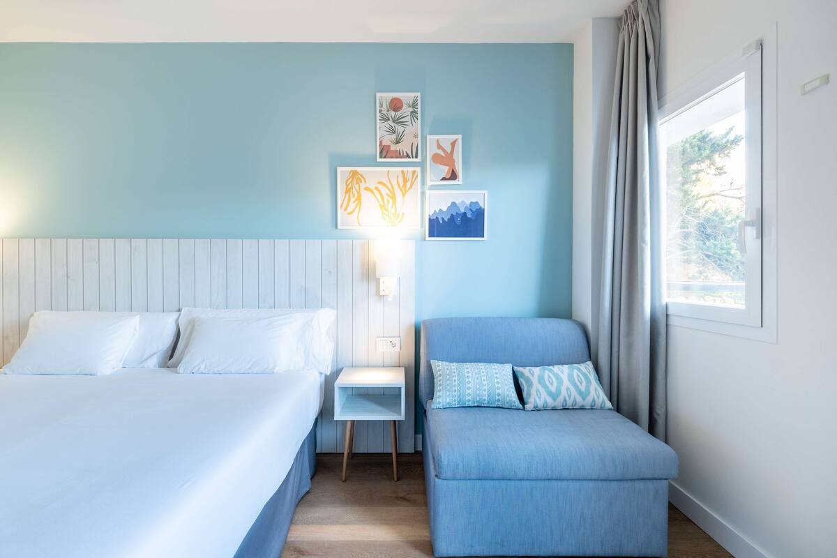 A bedroom with a bed, a nightstand, a blue sofa, and wall art.