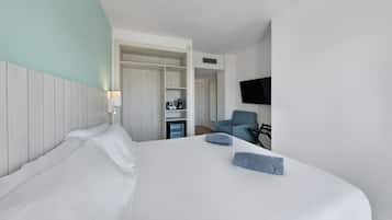 Quarto de hotel moderno com uma cama grande, uma escrivaninha com cadeira, televisão e minibar.