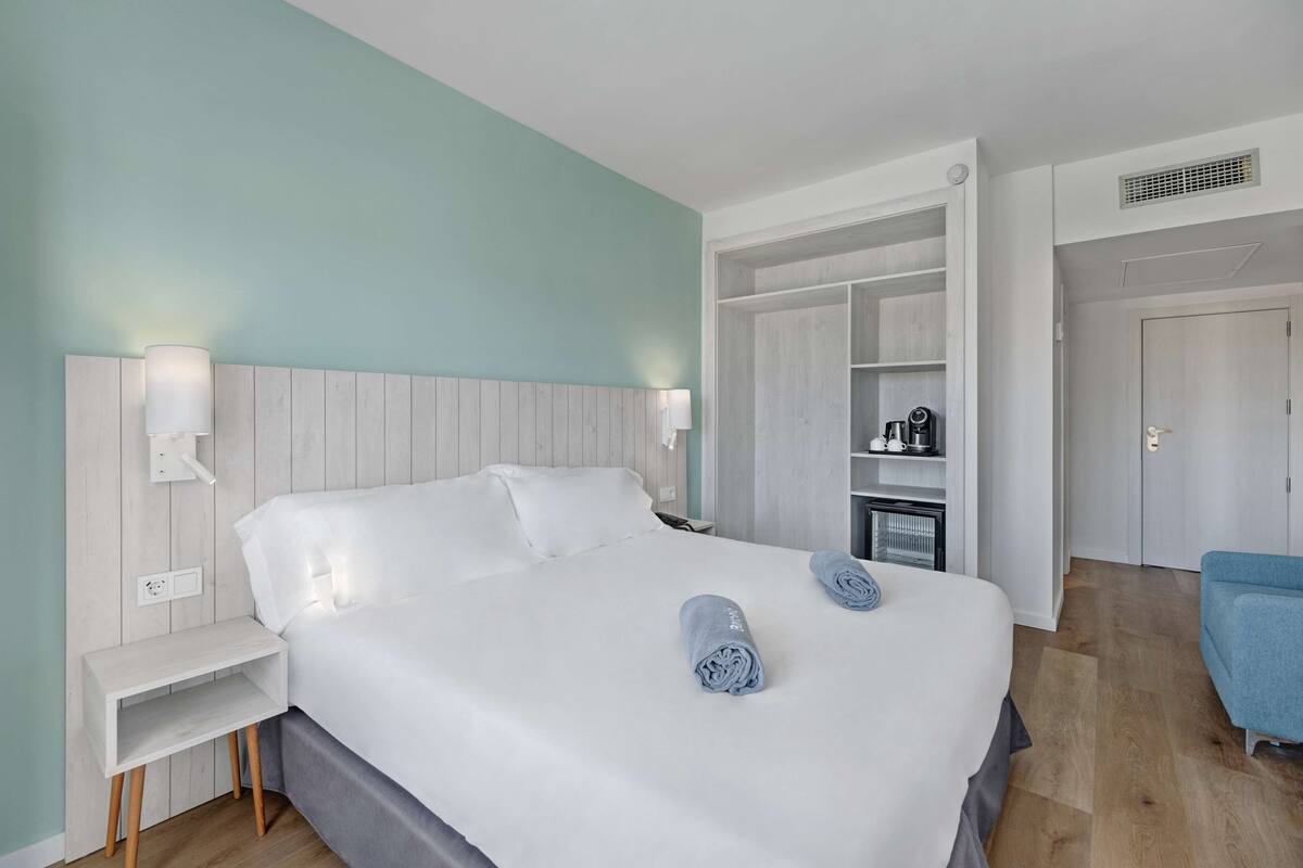 A modern hotel room with a large bed, bedside tables, a wardrobe, and a seating area.