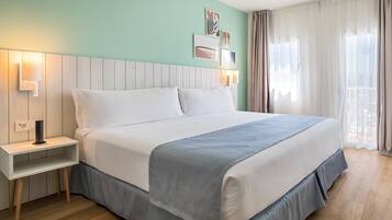A neatly made bed with a white headboard and a grey blanket, a bedside table with a lamp, and a wall-mounted picture frame.