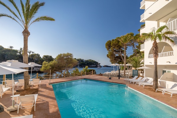 A pool area with lounge chairs and umbrellas, a clear view of the sea, and a building with balconies. - Barceló Ponent Beach (Felanitx)