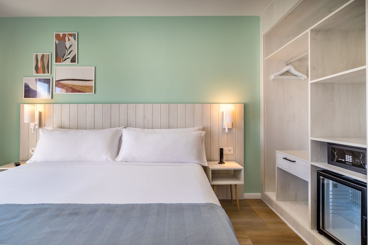 A neatly arranged hotel room with a large bed, bedside tables, a built-in wardrobe, and wall-mounted artwork.