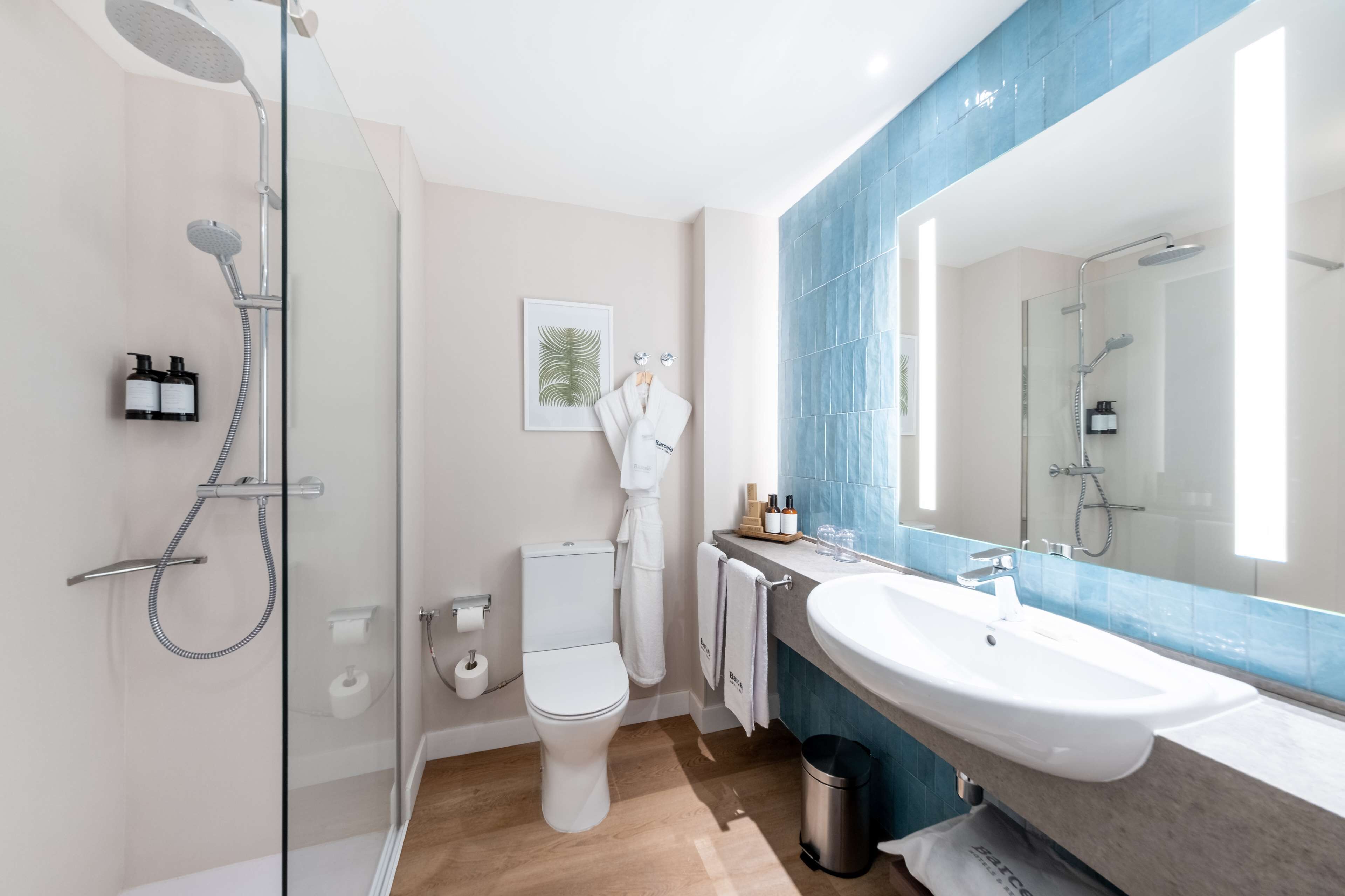 Une salle de bain moderne avec une douche en verre, des toilettes blanches, un grand lavabo et un miroir avec un pare-éclaboussures bleu.