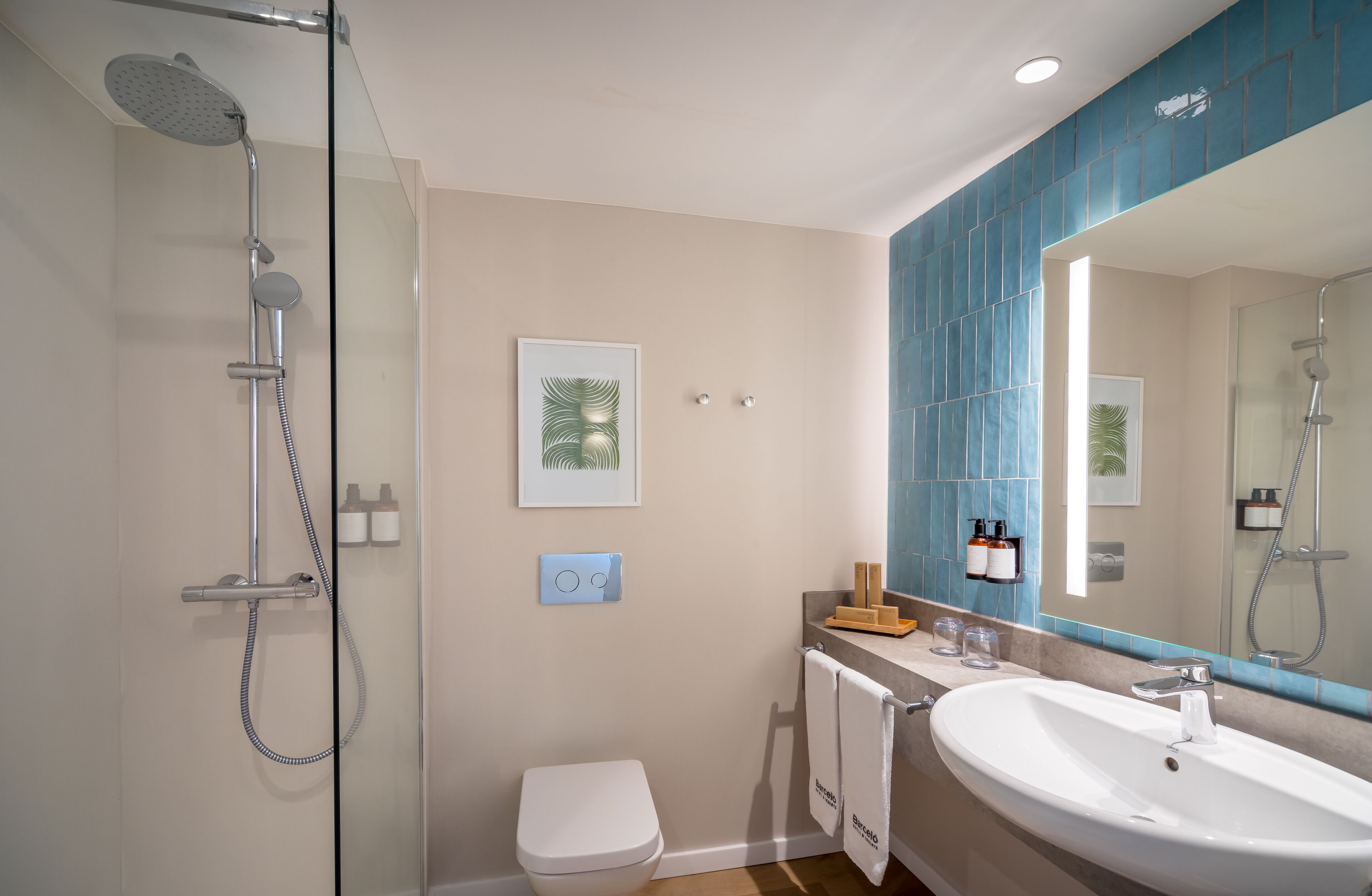 A modern bathroom with a glass-enclosed shower, a white toilet, a large sink, and a mirror with a blue-tiled backsplash.