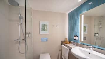 Un baño moderno con ducha de vidrio, inodoro blanco, lavamanos grande y espejo con zócalo de azulejos azules.