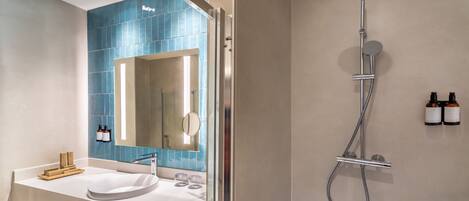 A modern bathroom with a white sink, a large mirror, and a shower with a handheld showerhead.