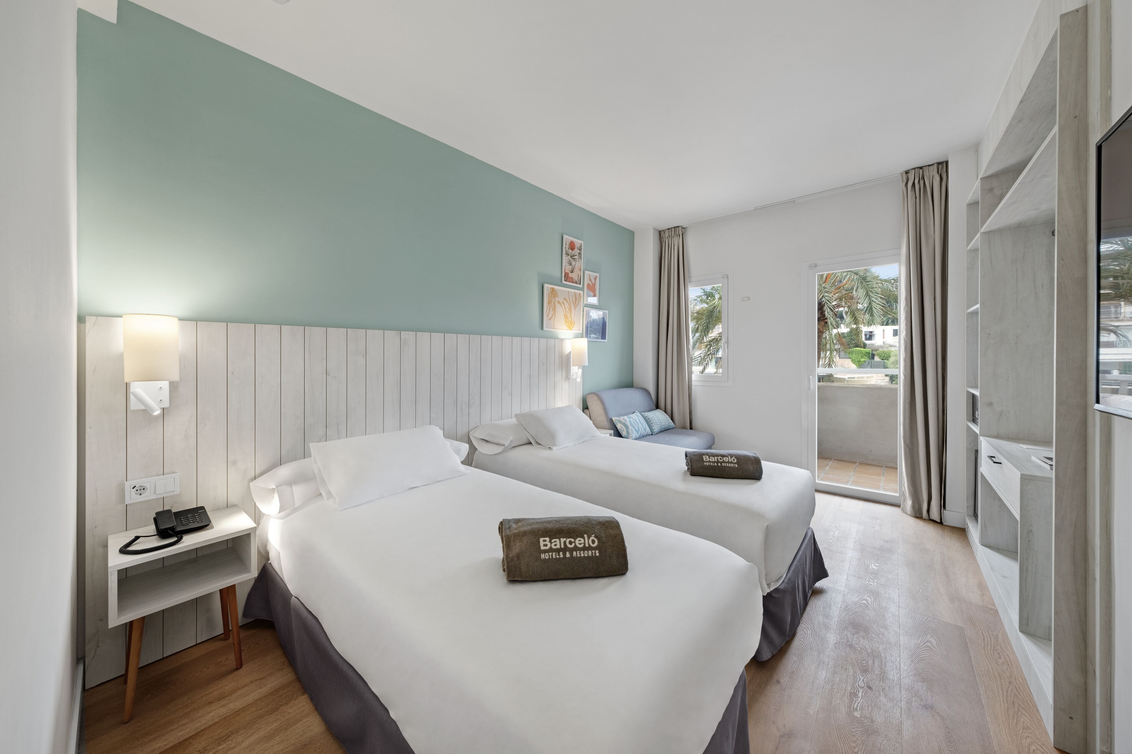 Een hotelkamer met twee bedden, een nachtkastje met telefoon, een wandlamp en uitzicht.