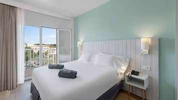 Habitación de hotel con una cama grande, una mesita de noche con teléfono y vistas a la ciudad a través de un amplio ventanal.