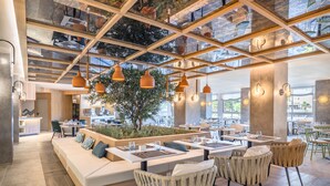 A modern restaurant with a high ceiling, wooden beams, hanging pendant lights, and a central seating area with a planter. - Barceló Ponent Beach (Felanitx)