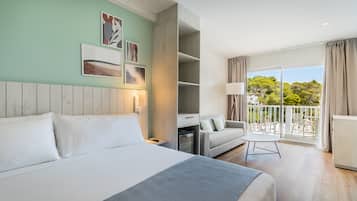 A modern hotel room with a large bed, a sofa, a balcony with a view, and artwork on the walls.
