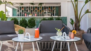 An outdoor seating area with two round tables, a bar in the background, and potted plants. - Barceló Ponent Beach (Felanitx)