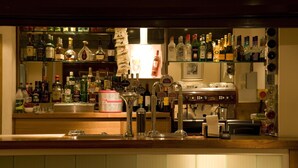 A bar area with shelves of liquor bottles, a bar counter, and a coffee machine. - Premier Inn London Kensington (London)