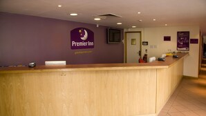 A hotel reception desk with a wooden counter, a sign for Premier Inn, and a fire extinguisher. - Premier Inn London Kensington (London)