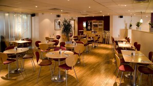 A restaurant with multiple tables and chairs, a bar area, and a large potted plant. - Premier Inn London Kensington (London)