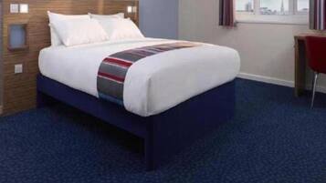 A hotel room with a bed, a desk, and a window.
