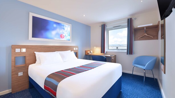 Une chambre d’hôtel avec un grand lit, un bureau, une chaise, une télévision et une fenêtre avec des rideaux.