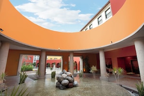 Un amplio patio con una formación rocosa en el centro, rodeado de columnas y plantas en macetas.
