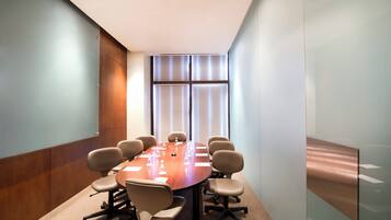A conference room with a wooden table, beige chairs, and a large window with blinds.