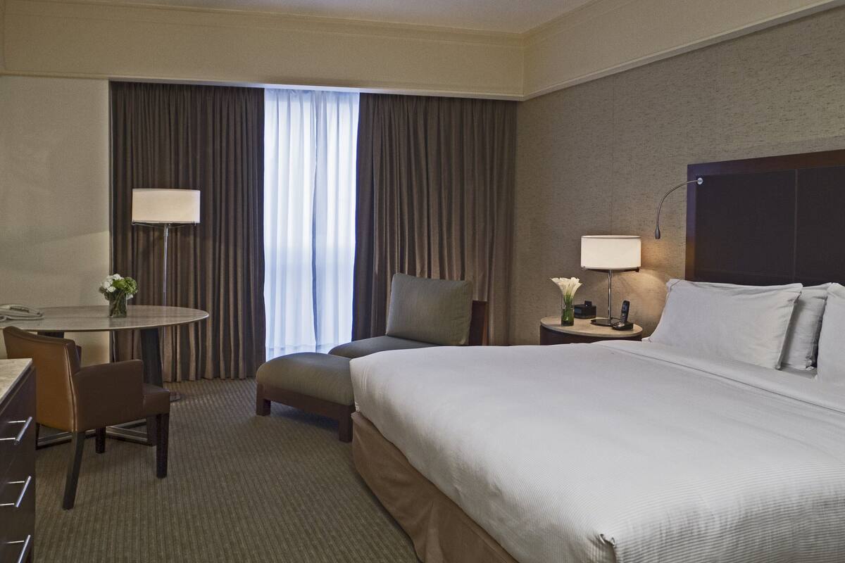 A hotel room with a bed, a desk, a chair, a lamp, and a window with curtains.