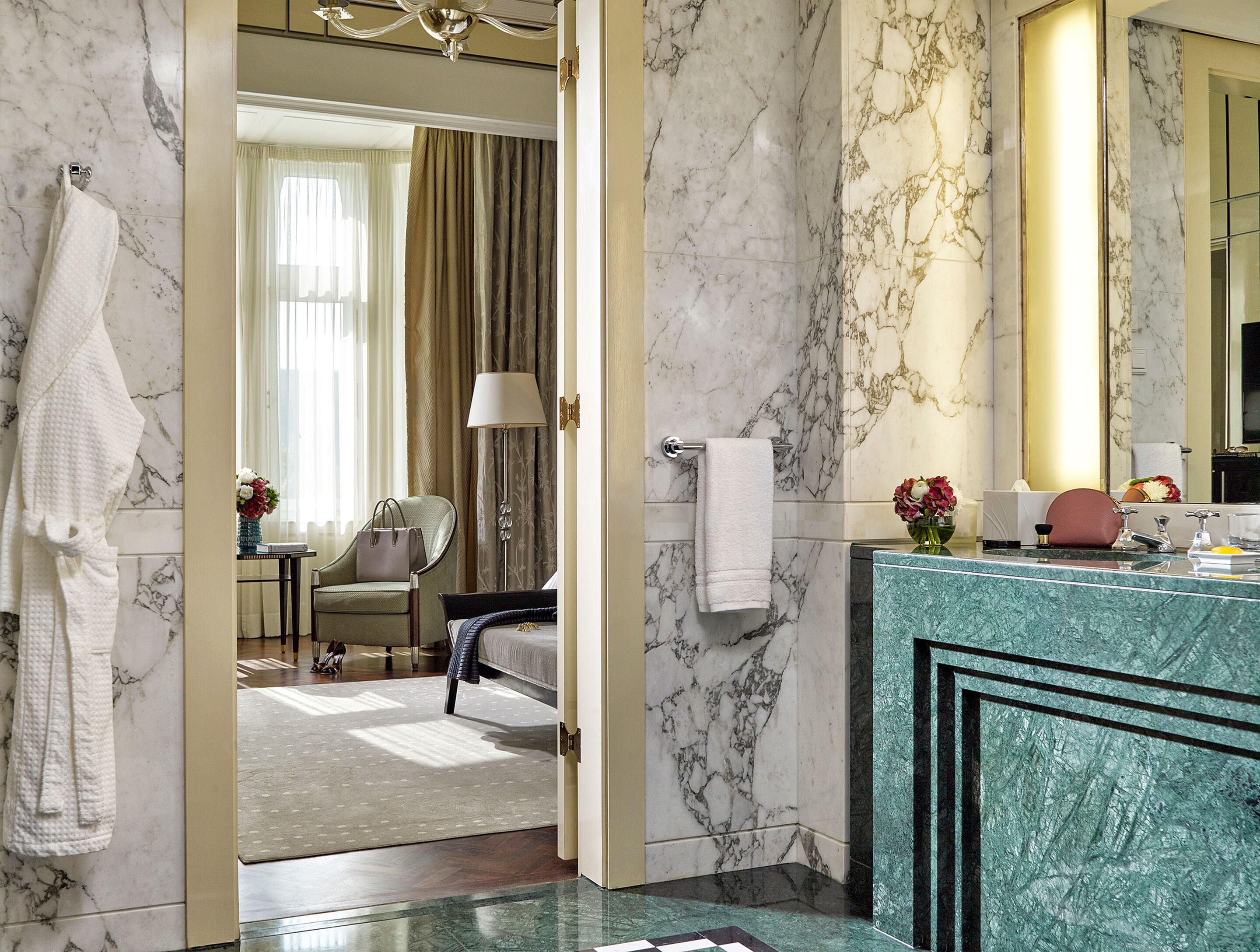 Een hotelbadkamer met marmeren wanden, een wastafel met een groen marmeren aanrechtblad, een spiegel en een handdoekrek.