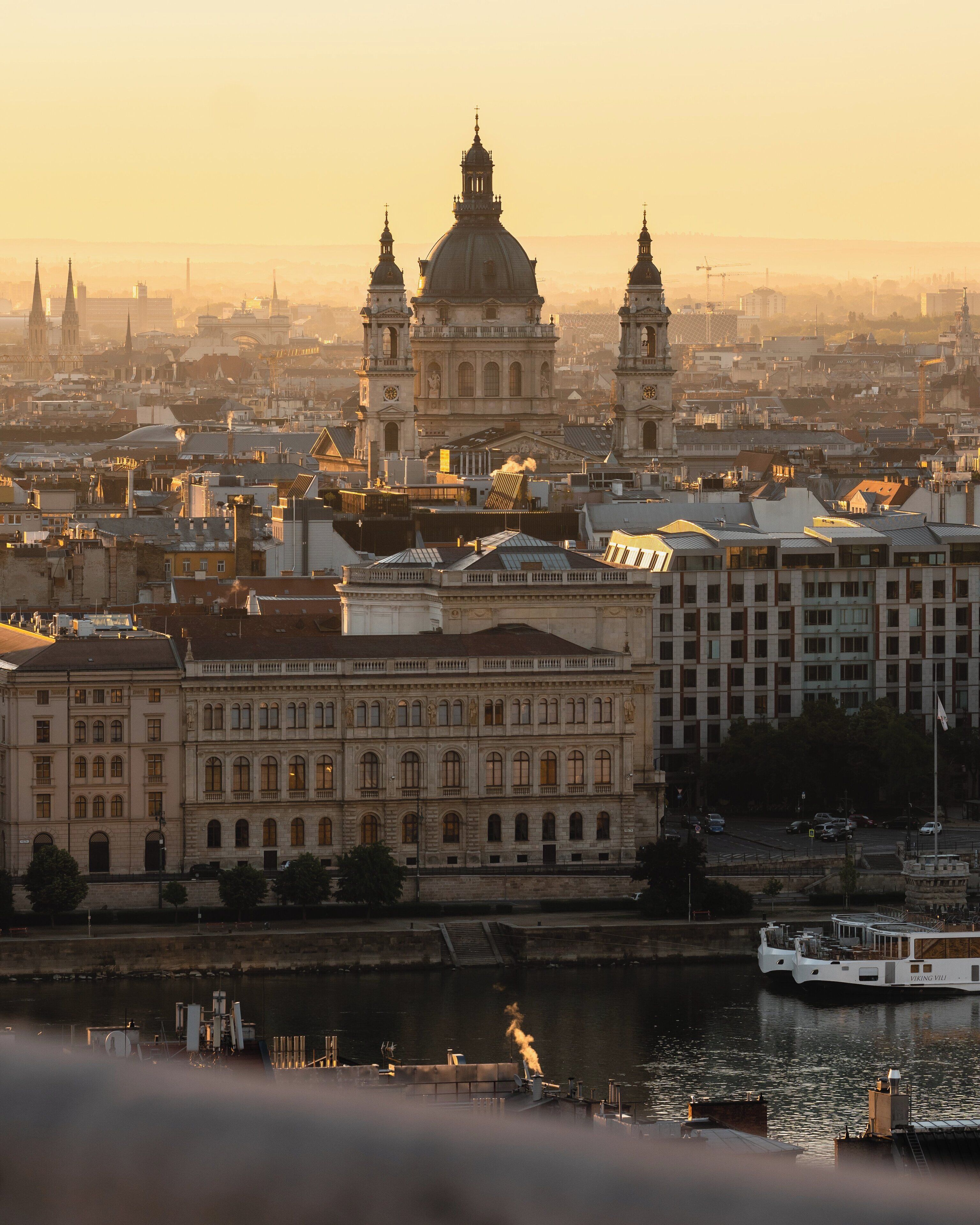 A historic building with classical architecture, a river, and a boat docked nearby.
