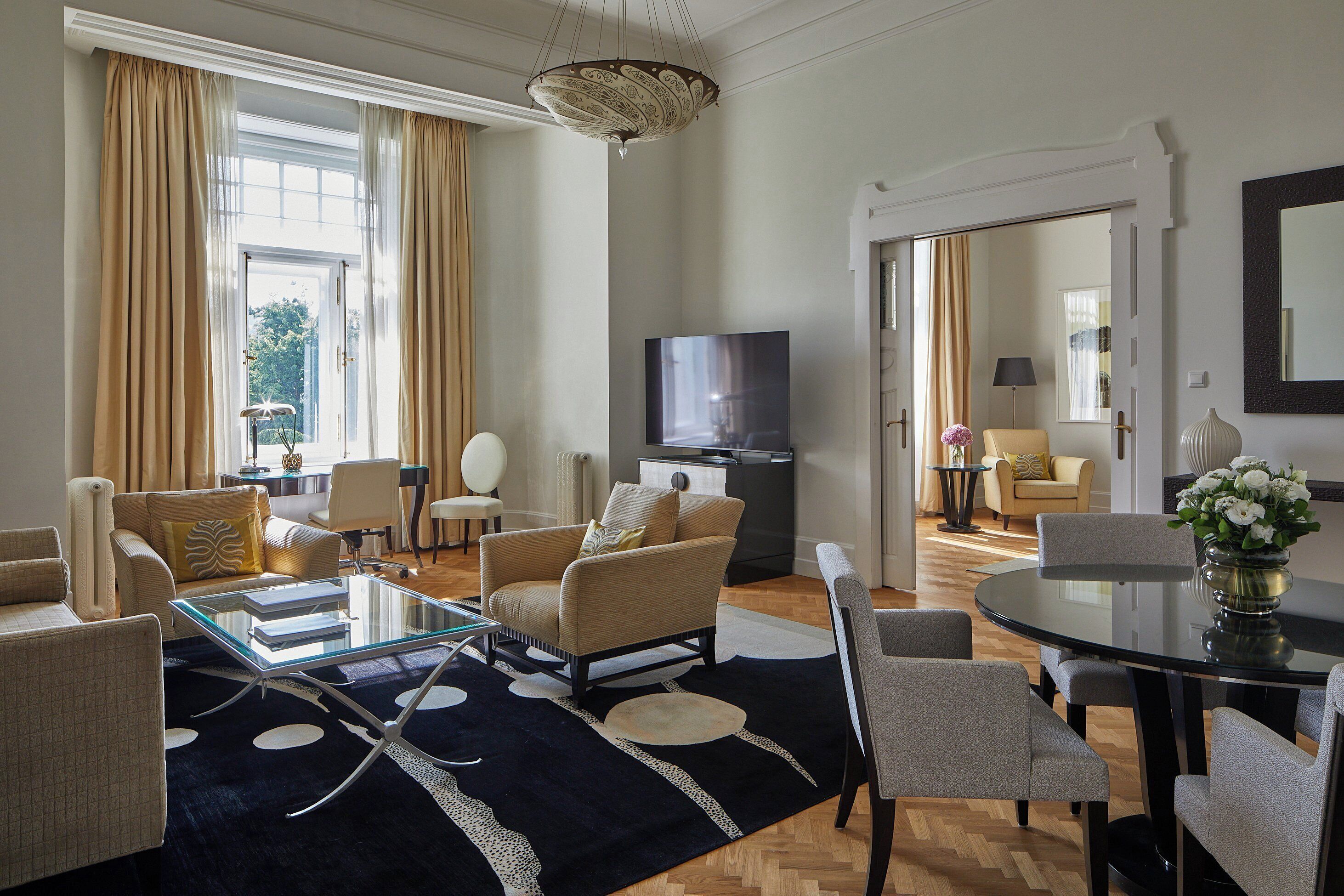 A spacious living room with a large window, a flat-screen TV, and a dining area with a round table and chairs.