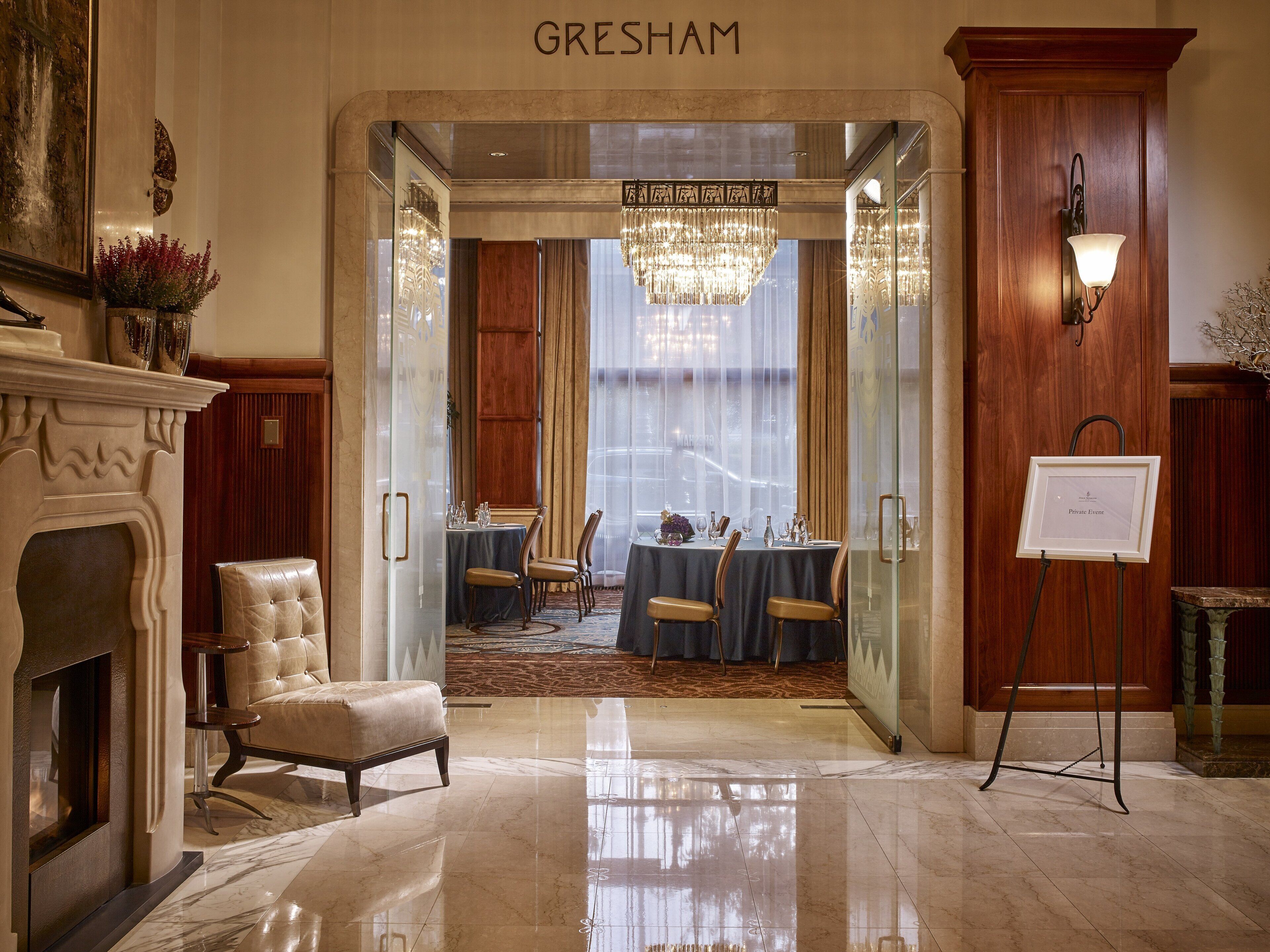 En lobby på Gresham Hotel med en marmorgulv, pejs, siddeområde med borde og stole, samt en lysekrone.